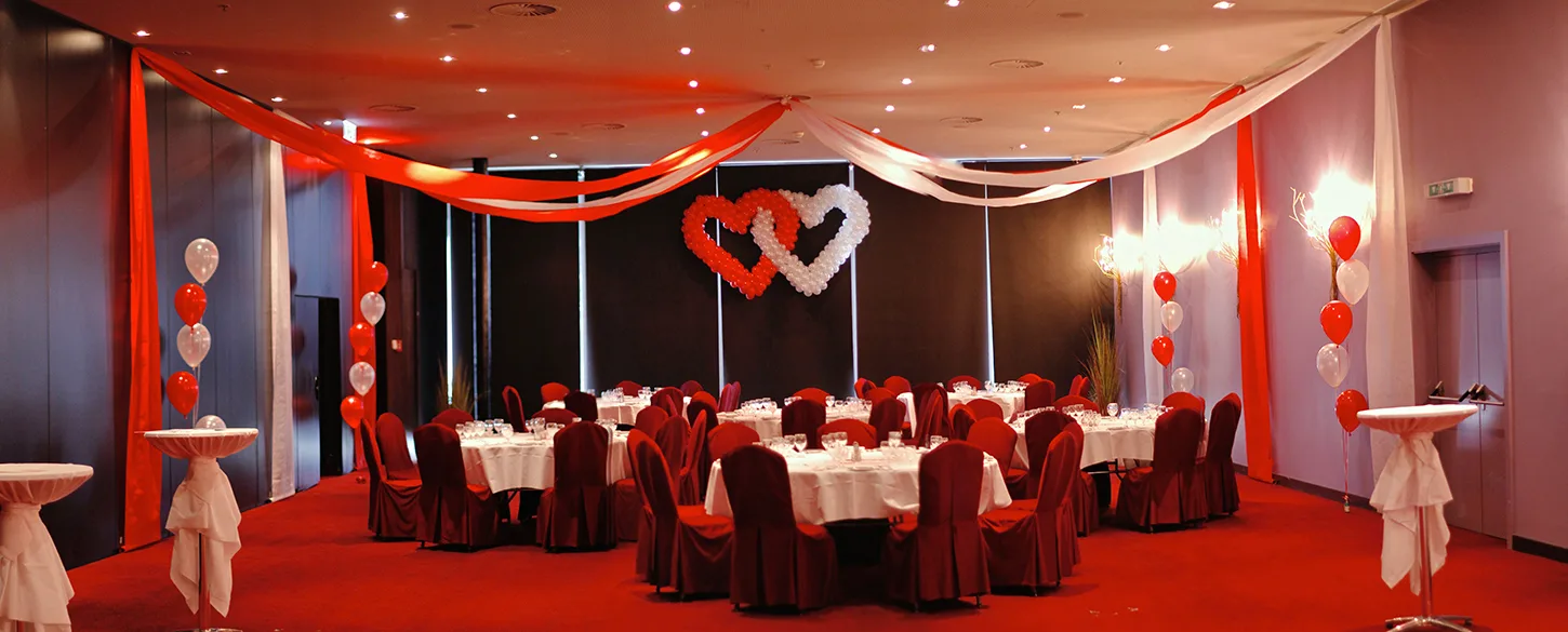 Salle décorée de drapés rouges et d'un double cœur en ballons